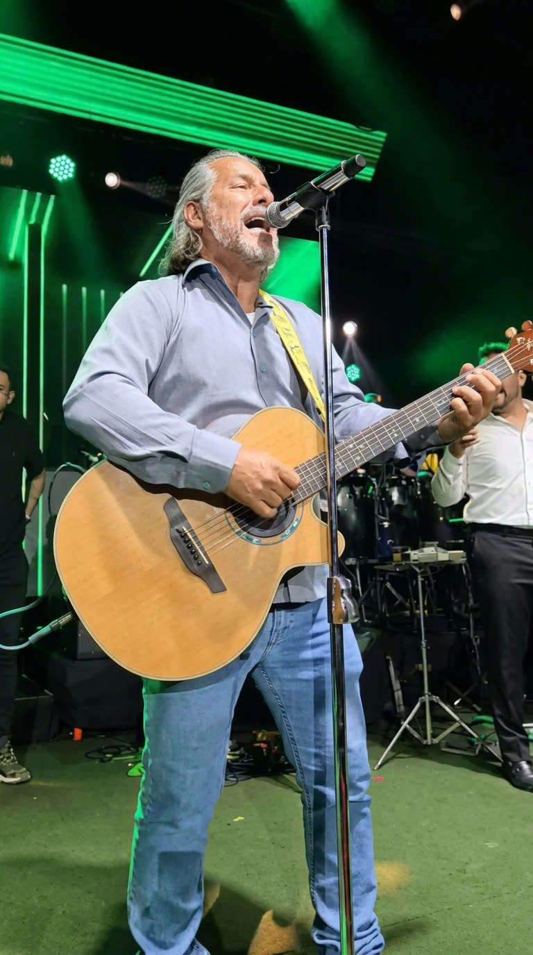 Gleno Rossi cantando ao vivo com violão sob luzes verdes de palco