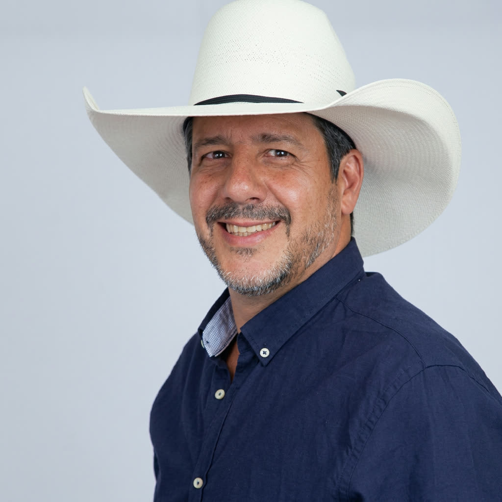 Retrato de Gleno Rossi sorrindo, de chapéu branco e camisa azul