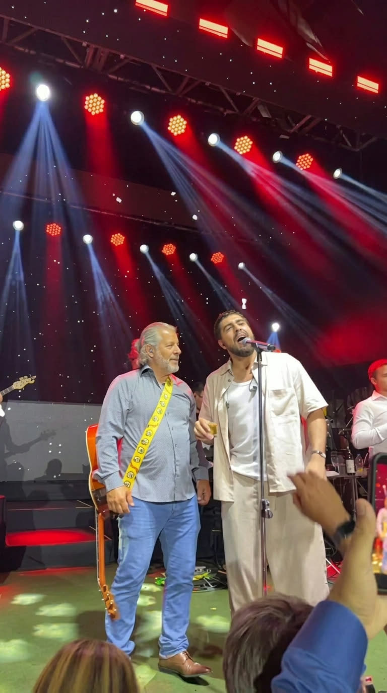 Gleno Rossi no palco ao lado de outro cantor, sob luzes vermelhas e azuis
